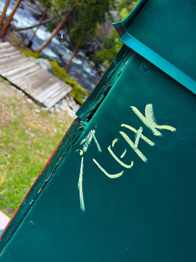 damaged green metal roof section with chalk marks indicating a visible leak point near the edge.