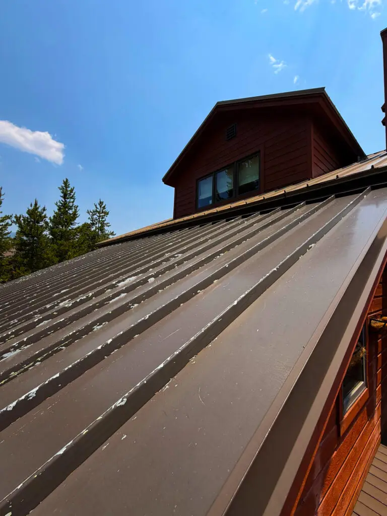 Weathered standing seam metal roof on a mountain home in Colorado, showing visible coating wear and roof surface damage.